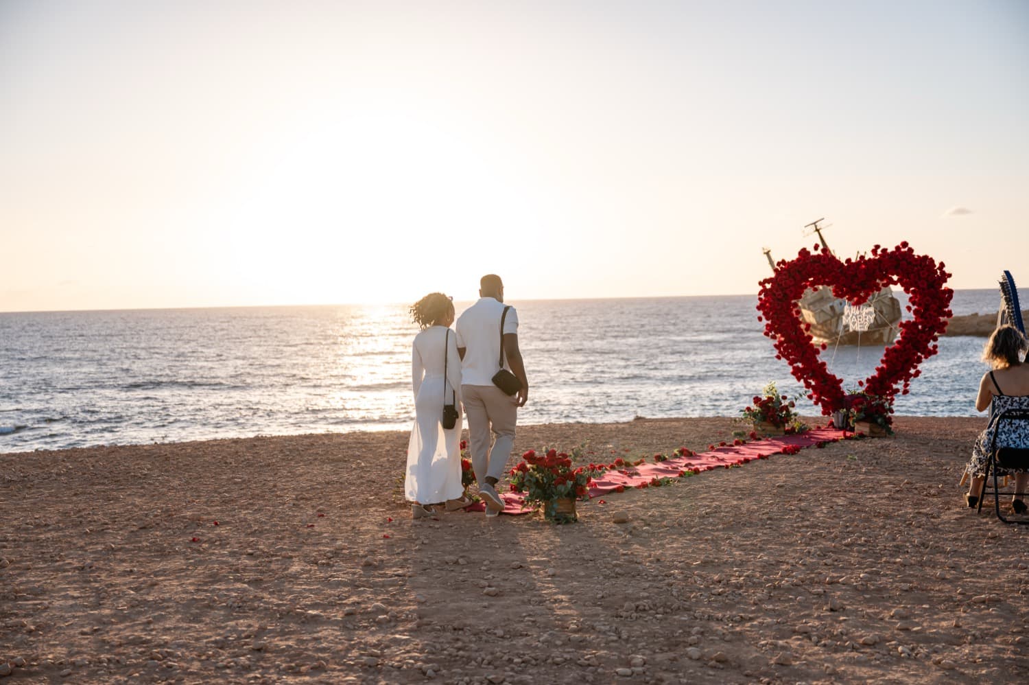 A couple silhouetted at sunset beside a proposal setup on the white rocks of the Cyprus coast