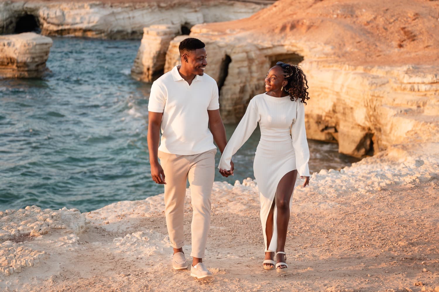 A couple walking hand in hand on the white sea-cave cliffs above the turquoise water in Cyprus